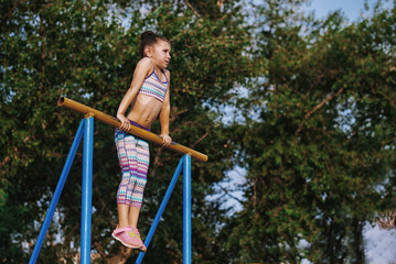 Sports girl on the bar in the summer in the park pulling on the bar