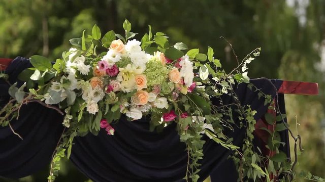 Wedding decorations for outdoor wedding ceremony. Wooden arch decorated with white and pink roses. Bees and bumblebees flying around natural flowers