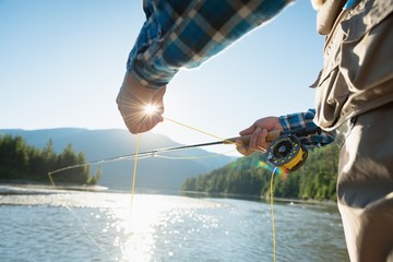 Mid section of man holding thread while fishing in river