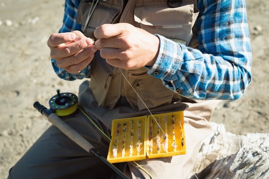 Mid section of man tying fishing hook on rod while sitting on