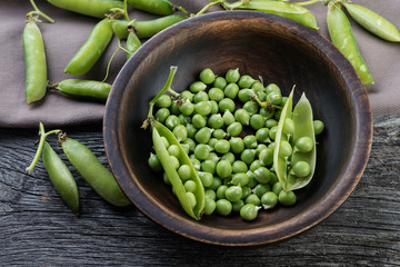 fresh peas in a wooden bowl on a rustic wood background
