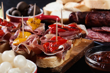 Spanish tapas with slices jamon serrano and grilled pepper. Also olives, salami, pickled onions, and peppers stuffed with cheese