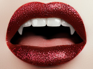 Female lips with glittering red lipstick, vampire teeth - obrazy, fototapety, plakaty