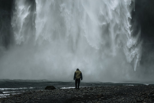 Male in jacket standing in front of gigantig skogafoss waterfall in iceland