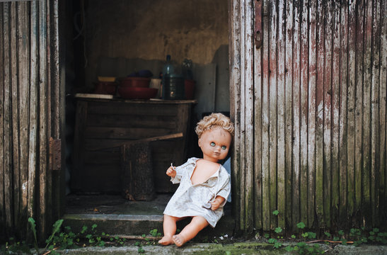 The old doll is left in the doorway of an old abandoned building. Fear of loneliness. Vintage background.