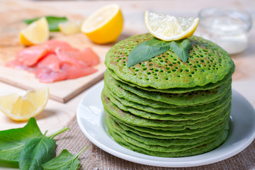 A stack of pancakes of spinach. On the table along with the fish, spinach and lemon wedges.