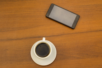 Fototapeta na wymiar Cup of coffee and smartphone on wooden table. Top view