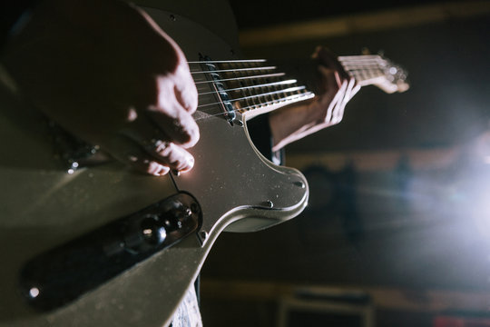 Playing electric guitar in studio closeup. Unrecognizable guitarist, music recording process, dark atmosphere with back light