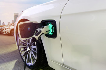 Electric Car Charging on parking lot with Electric car charging station on city street.  Close up of power supply plugged into  Electric car being charged with green light display status full battery.