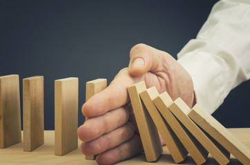 Businessman halting the domino effect inserting his hand between falling and upright wooden blocks