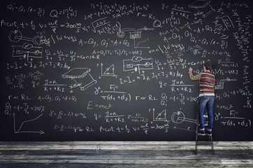 Student writing on blackboard formulas from many different subjects