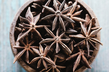 Whole star anise in a bowl on blue wooden background, top view