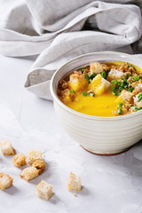 Mug of vegetarian pumpkin carrot soup served with croutons and onion on textile napkin over gray concrete background. Close up