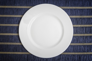 Empty white plate on blue tablecloth background