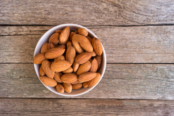 White ceramic bowl with almonds on the wooden background
