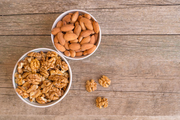 Two ceramic bowls full of walnuts and almonds on the wooden table