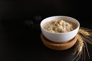 Oat porridge with blackberries, ears of corn on a dark background