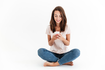 Smiling brunette woman sitting on the floor and using smartphone