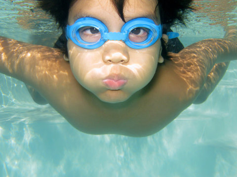 Underwater healthy active young boy fun in swimming pool with goggles. Little Asian kid swimming under water holding breath. Child diving, summer vacation, pool activities or sport concept.
