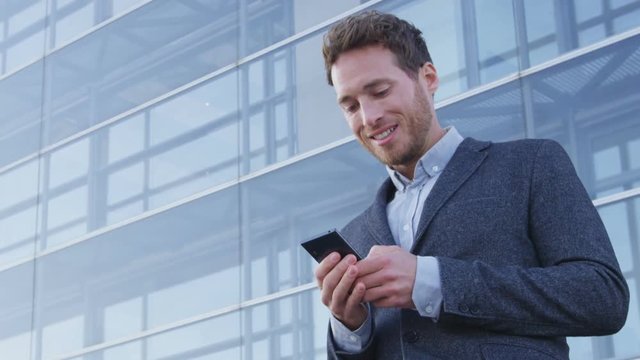 Man sms texting using app on smart phone in city business district. Young business man using smartphone smiling happy wearing suit jacket outdoors. Urban male professional in her 20s. RED EPIC.