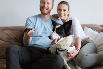 Beautiful couple watching television at home with their dog