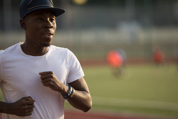 African male sportsman in a cap running on stadium track, he trains endurance