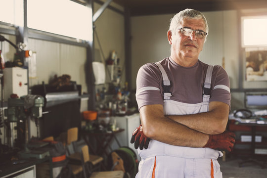 Senior man in workshop.  Man poses a crossed arm in a workshop and looks at the camera