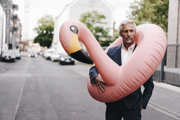 Mature businessman on the street with inflatable flamingo