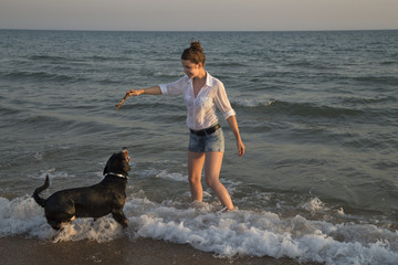 Beautiful young woman playing with her dog on the beach.