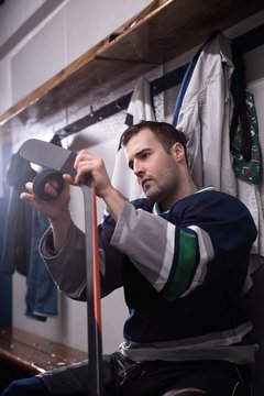 Male player taping hockey stick and puck in locker room