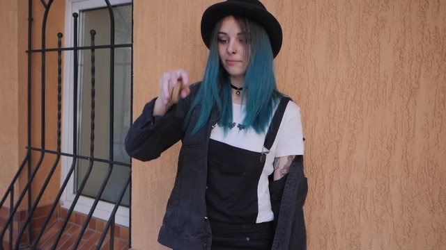 SLOW MOTION: emo girl playing with old school toy yo yo. Street punk or hipster with blue dyed hair,piercing,lenses,tattooed,ears tunnels and unusual hairstyle stands in backyard.