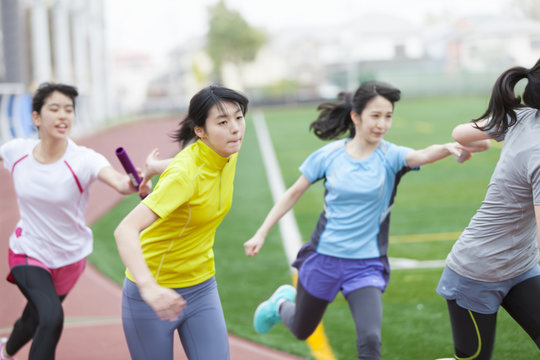 Female students on athletic trackpassing batons