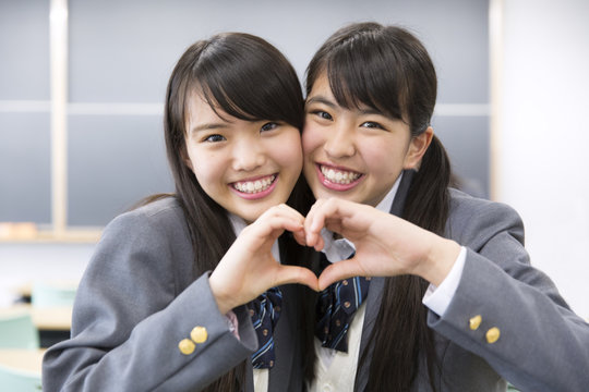 Two high school girls in a classroommakeing heart shape by hand