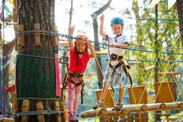 Portrait of cute little boy and girl walk on a rope bridge in an adventure rope park.