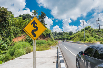 Yellow sign with winding road symbol in the countryside and sky background .