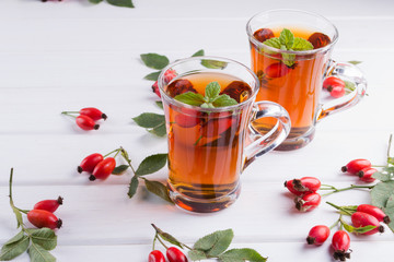Rose hip tea in transparent cup with honey and fresh berries. Vitamin C drink on white background.