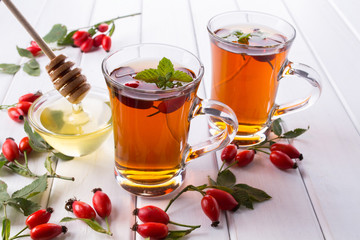 Rose hip tea in transparent cup with honey and fresh berries. Vitamin C drink on white  background.