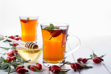 Rose hip tea in transparent cup with honey and fresh berries. Vitamin C drink on white  background.