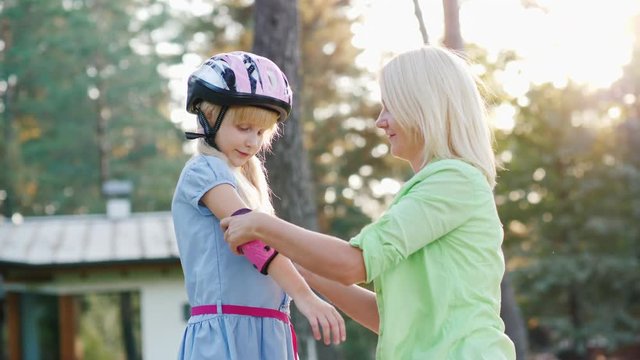 Slow motion shot: Mom dresses daughters of elbow pads for cycling or roller skates. Parent care