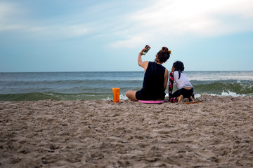 Mother and daughter enjoying vacation taking picture on cell phone by the beach