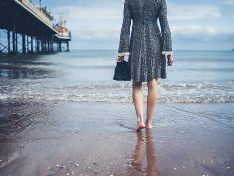 Woman walking on beach with shoes in hand
