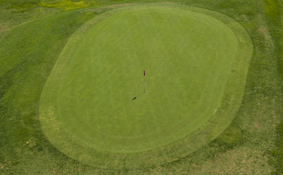 Vista aerea di un campo da golf. Nel dettaglio si vede il prato della buca finale e la bandiera rossa di segnalazione. Il sole splende ed è una giornata ideale per fare sport e stare alla aria aperta.