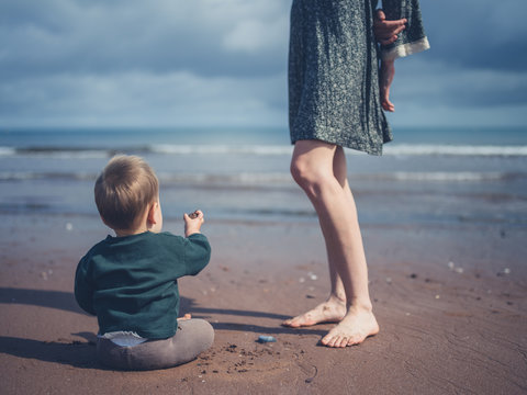 Little baby playing by legs of mother on beach