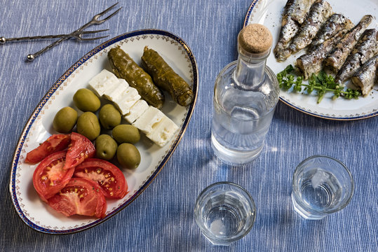 Two glasses and bottle of traditional drink Ouzo or Raki and appetizers on blue matting