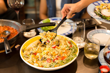 Family dinner hand with big spoon eating pasta salad with cherry tomato and sunflower sprouts
