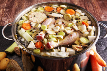 Bone broth made from chicken with carrots, onions various fresh vegetables in a pot - colorful fresh clear spring soup. Rural kitchen scenery bouillon or stock