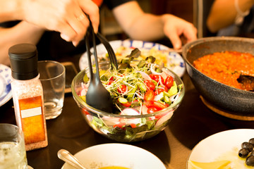 Family dinner hand holding big spoon with fresh vegetable salad in glass bowl