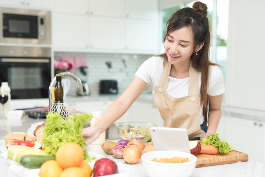 Portrait of young asian girl try to reach the ingredients on the table while cooking salad for her meal