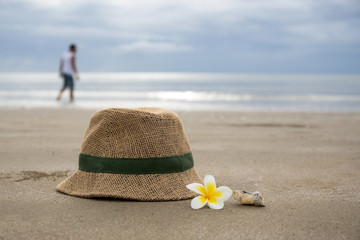 Hat with frangipani flower and people in background