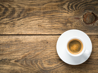 black frothy coffee with foam in white cup with saucer on aged wooden background